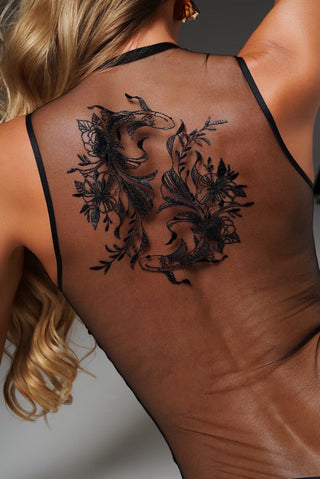 A black temporary tattoo of two koi fish intertwined with floral elements, shown on the back of a woman's upper back.