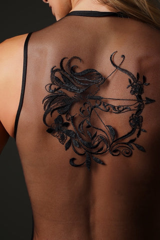 A black temporary tattoo of a female archer with floral details applied to a woman's upper back, shown from behind.
