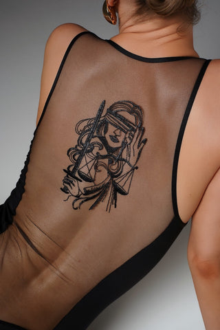 A woman shown from the back wearing a black sheer mesh bodysuit, displaying a large black line-art graphic of a blindfolded woman holding a sword on her upper back.