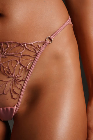 Close-up of a model wearing a dusty rose pink lace thong with a matching satin waistband and a small silver ring connector.