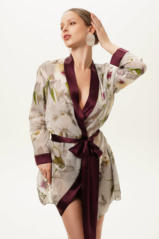 Woman wearing a floral silk robe kimono with a deep neckline and burgundy trim on a white background