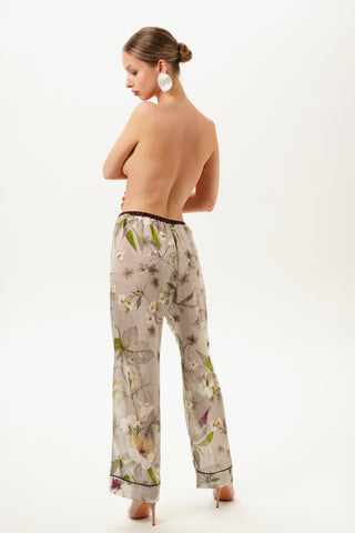 Back of a woman wearing floral printed silk pajama pants on a white background