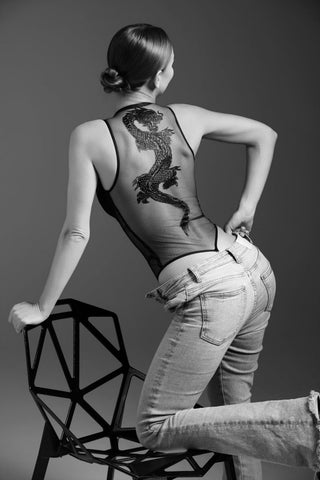 Person sitting on a modern chair with a geometric design, wearing a tank top with a dragon pattern and jeans.